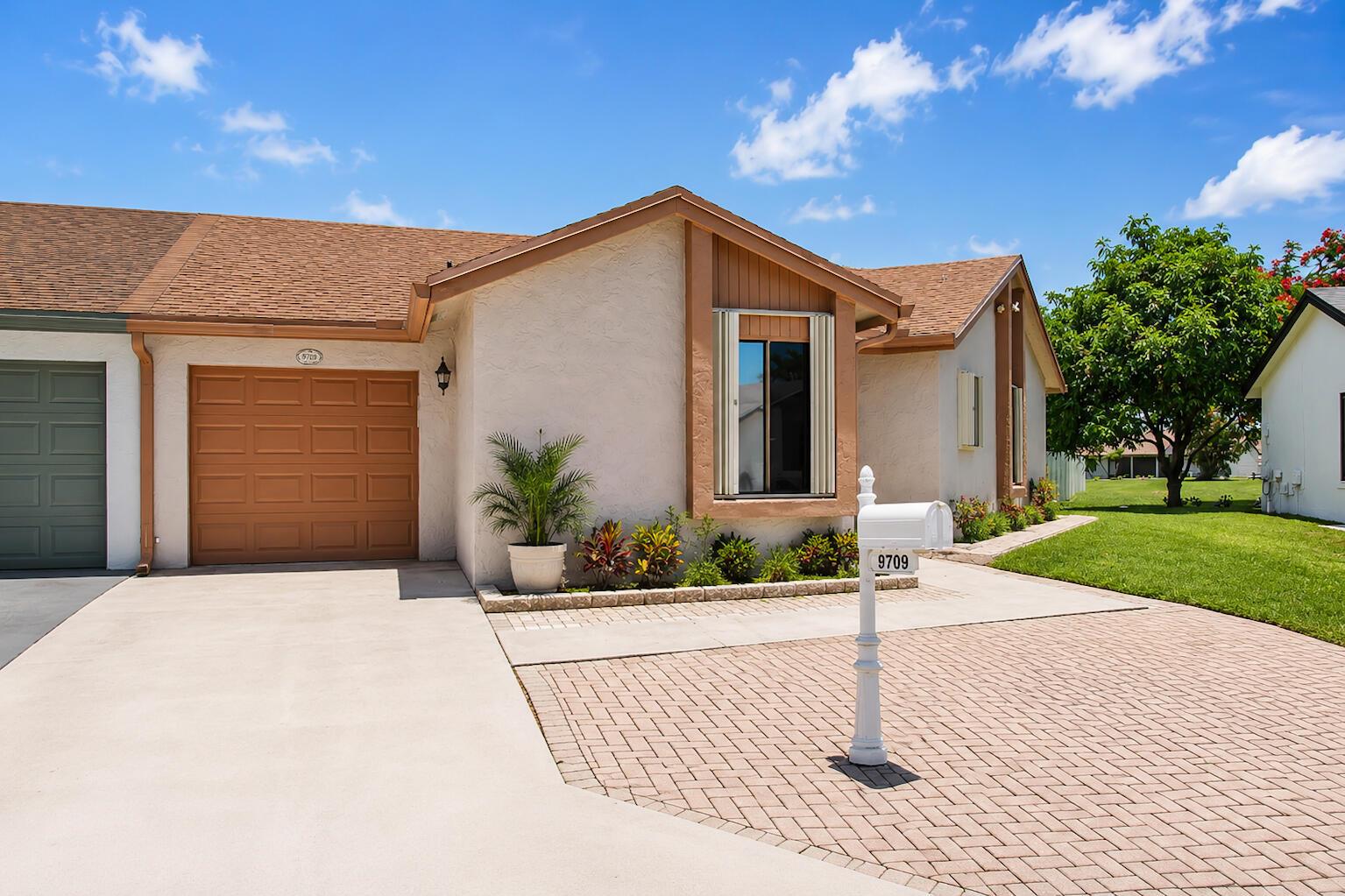 A single-story house exterior features a brown garage door, a paved driveway, and a mailbox — 9709 Sunny Isle Circle, Boca Raton FL 33428, BOCA RATON, FL