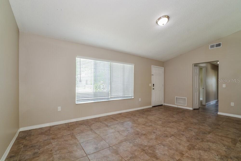An empty room features tan walls, a large window with blinds, and brown tile flooring — 5343 BROKEN PINE CIRCLE, ORLANDO, FL