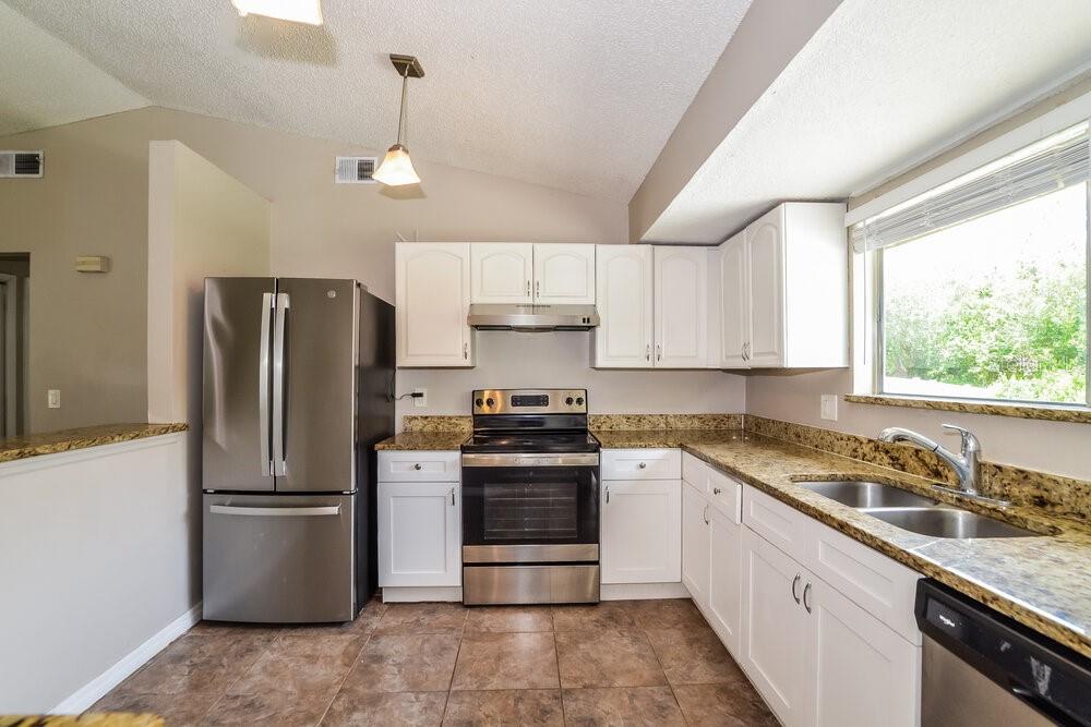 A kitchen with white cabinets, granite countertops, stainless steel appliances, and brown tile flooring — 5343 BROKEN PINE CIRCLE, ORLANDO, FL