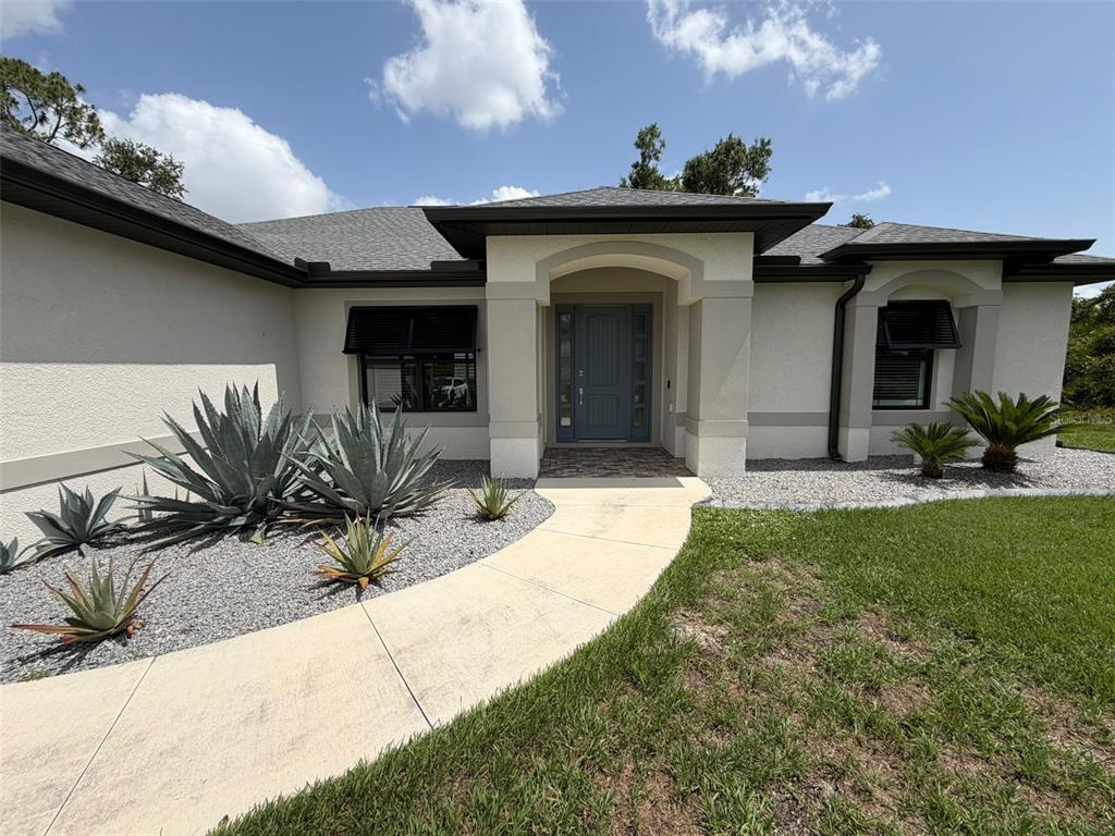 A single-story house with a beige stucco exterior, a gray front door, and desert-style landscaping — 218 COUGAR WAY, ROTONDA WEST, FL