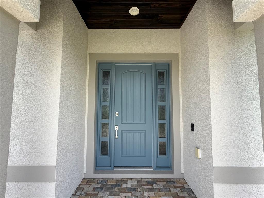 A blue front door with sidelights is set within a covered entryway with stucco walls — 218 COUGAR WAY, ROTONDA WEST, FL