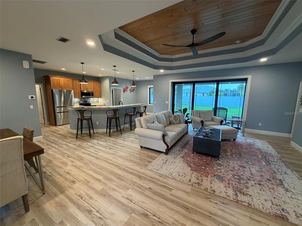 An open-concept living room and kitchen featuring wood-look flooring, a tray ceiling, and sliding doors — 218 COUGAR WAY, ROTONDA WEST, FL