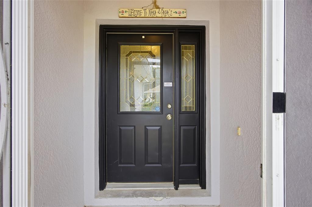 A black front door with a glass insert and sidelight sits under a welcome sign — 4905 KELSO STREET, LEESBURG, FL
