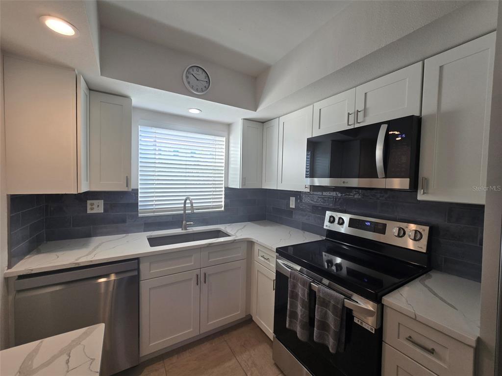 A kitchen features white cabinets, stainless steel appliances, a dark tile backsplash, and quartz countertops — 9200 MIDNIGHT PASS ROAD UNIT 10, SARASOTA, FL