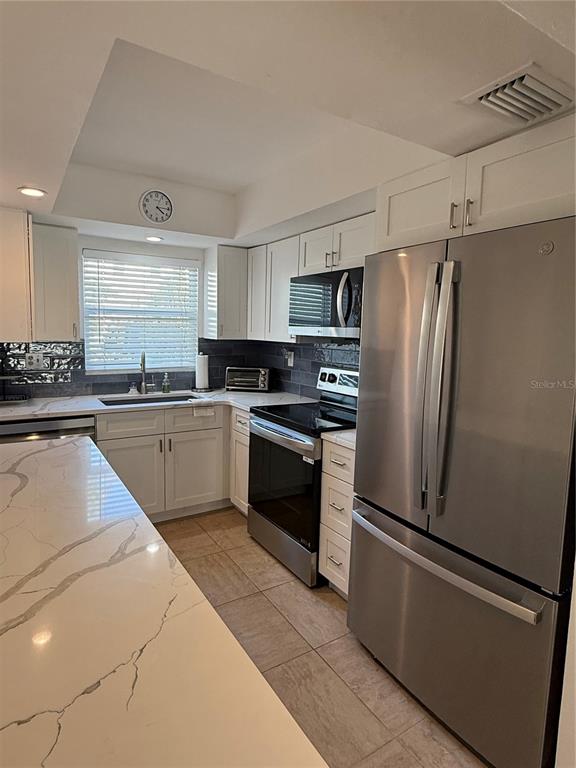 A kitchen features stainless steel appliances, white cabinets, and a large quartz-topped island — 9200 MIDNIGHT PASS ROAD UNIT 10, SARASOTA, FL