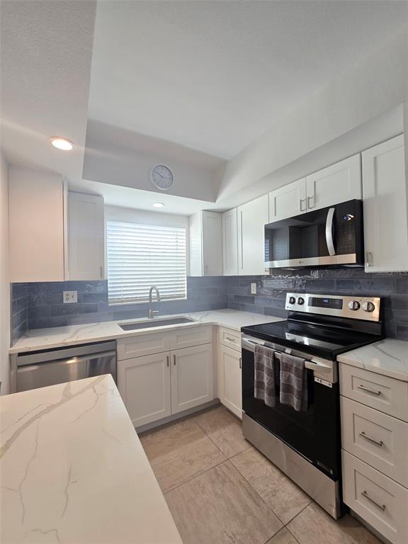 A kitchen features white cabinets, marble-look countertops, stainless steel appliances, and blue subway tile backsplash — 9200 MIDNIGHT PASS ROAD UNIT 10, SARASOTA, FL