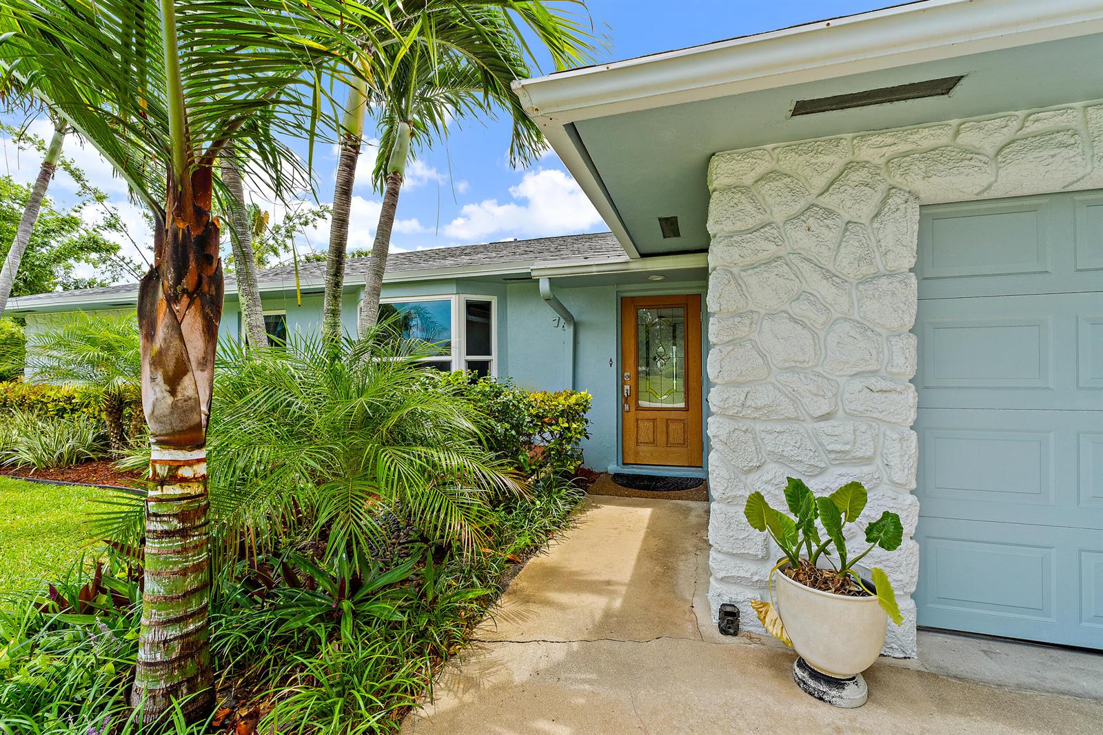A light blue house exterior features a stone facade, a wooden front door, and palm trees — 76 Wingo Street, Tequesta FL 33469, TEQUESTA, FL