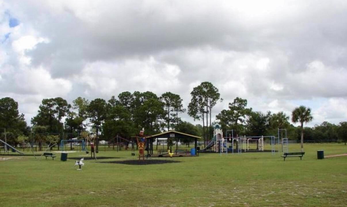 A playground with various equipment sits on a grassy field under a cloudy sky — 324 Pine Cone Avenue, Clewiston FL 33440, CLEWISTON, FL