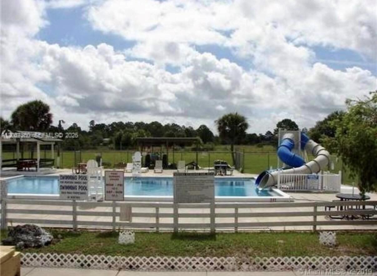 An outdoor swimming pool with a blue slide is enclosed by a white fence — 324 Pine Cone Avenue, Clewiston FL 33440, CLEWISTON, FL