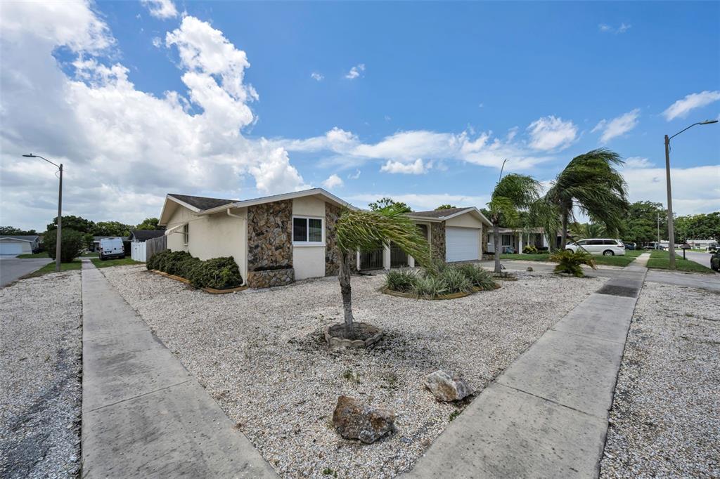 A single-story house with a stone facade and gravel yard sits on a corner lot — 5834 EMBAY AVENUE, NEW PORT RICHEY, FL