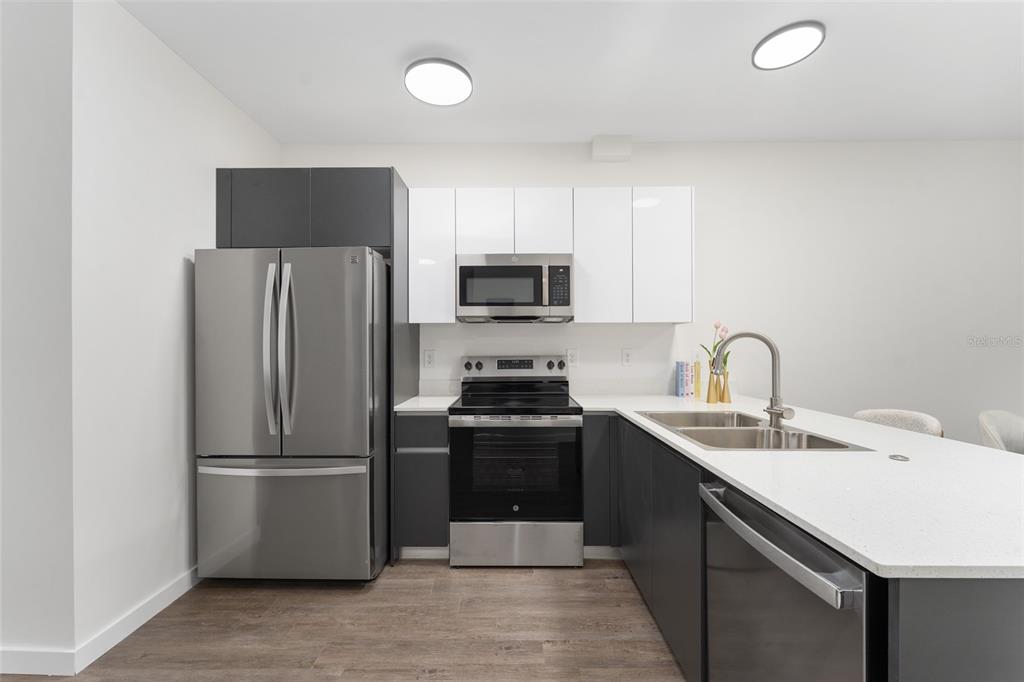 A modern kitchen features dark grey lower cabinets, white upper cabinets, and stainless steel appliances — 1581 NW 29TH ROAD UNIT 8, GAINESVILLE, FL
