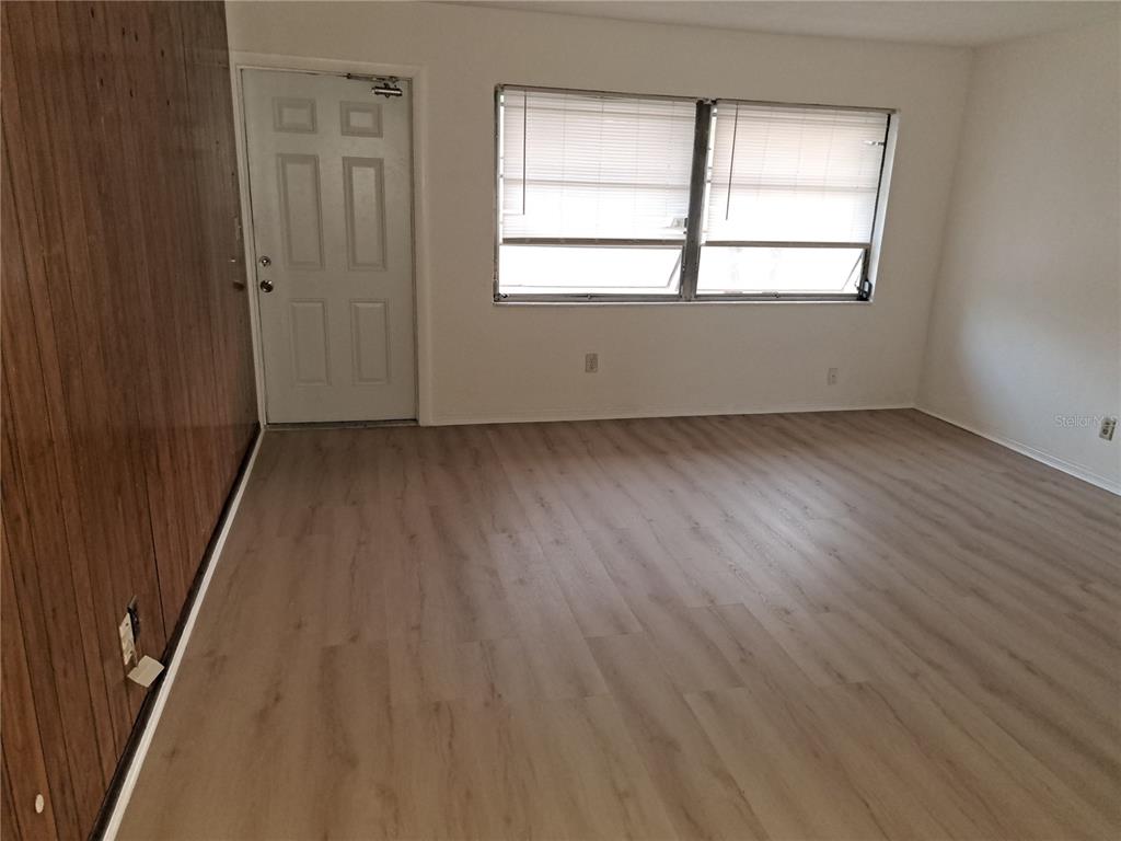 An empty room features light wood-look flooring, white walls, a white door, and a window — 4150 BARRACUDA DRIVE SE, ST PETERSBURG, FL