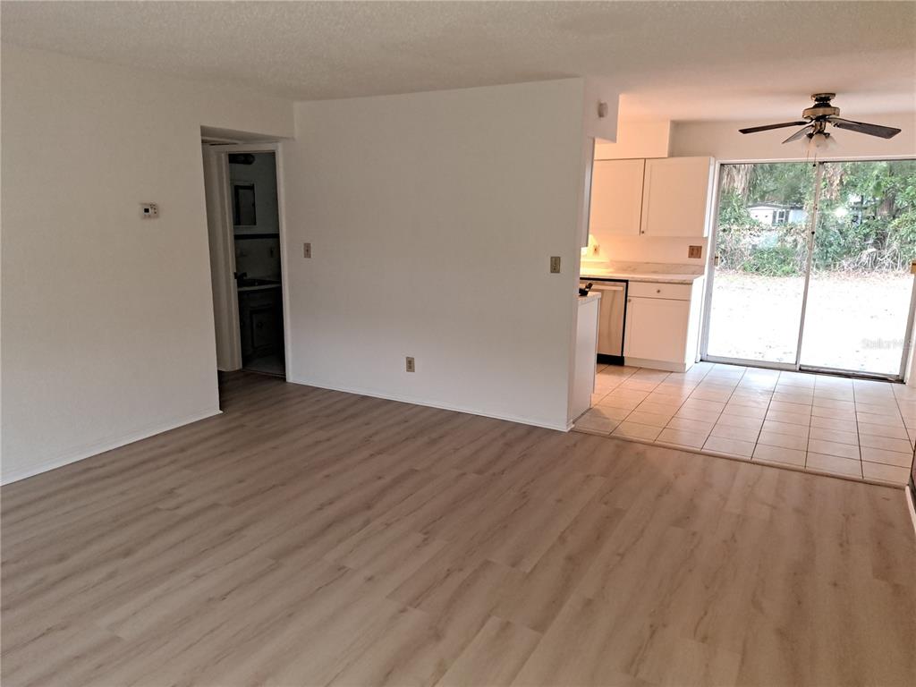 A living room with light wood-look flooring transitions to a tiled kitchen with white cabinets — 4150 BARRACUDA DRIVE SE, ST PETERSBURG, FL