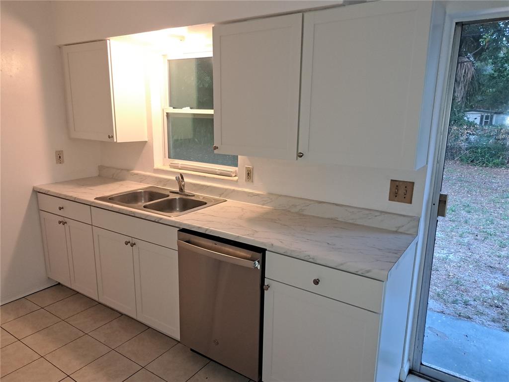 A kitchen features white cabinets, marble-patterned countertops, a stainless steel dishwasher, and a glass door — 4150 BARRACUDA DRIVE SE, ST PETERSBURG, FL