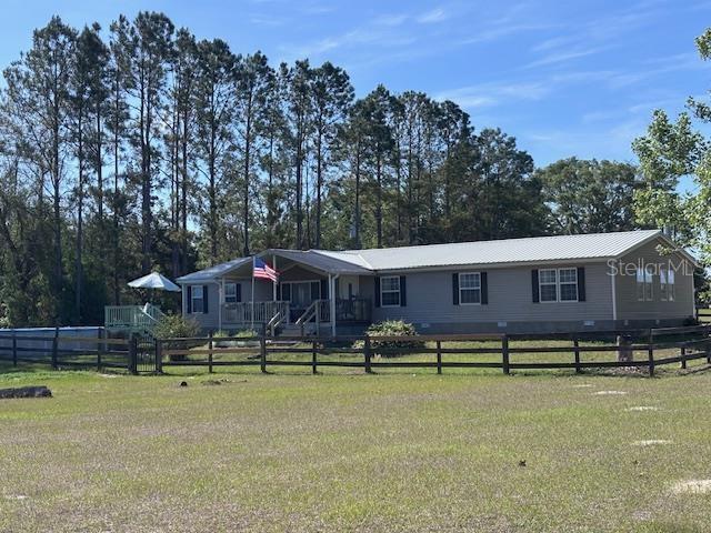 A single-story manufactured home with a metal roof sits behind a wooden fence — 10250 NW 67TH PLACE, CHIEFLAND, FL