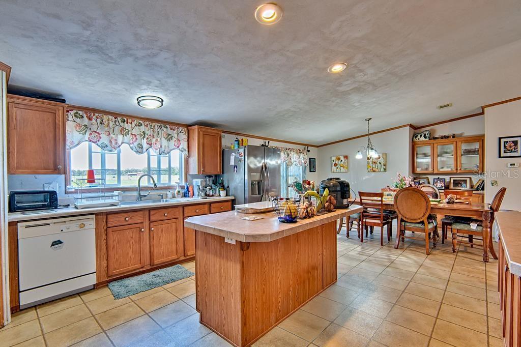 A kitchen with wood cabinets, a center island, tile flooring, and an adjacent dining area — 10250 NW 67TH PLACE, CHIEFLAND, FL