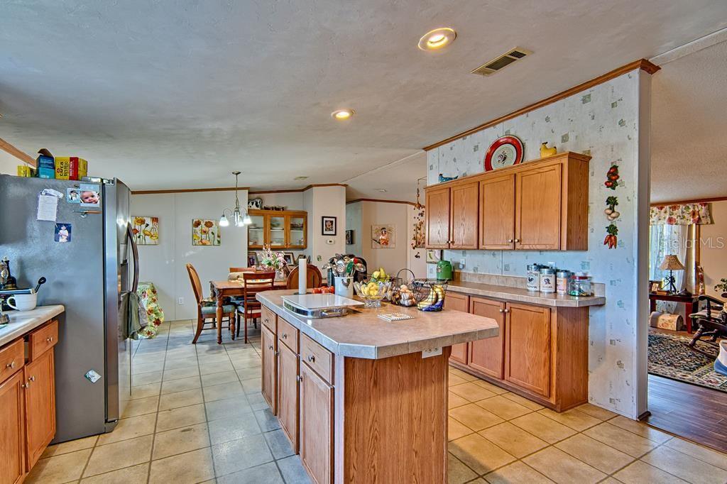 A kitchen with wood cabinets, a central island, and tile flooring opens to a dining area — 10250 NW 67TH PLACE, CHIEFLAND, FL