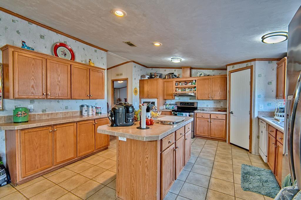 A kitchen features oak cabinets, tile countertops, a central island, and light-colored floor tiles — 10250 NW 67TH PLACE, CHIEFLAND, FL