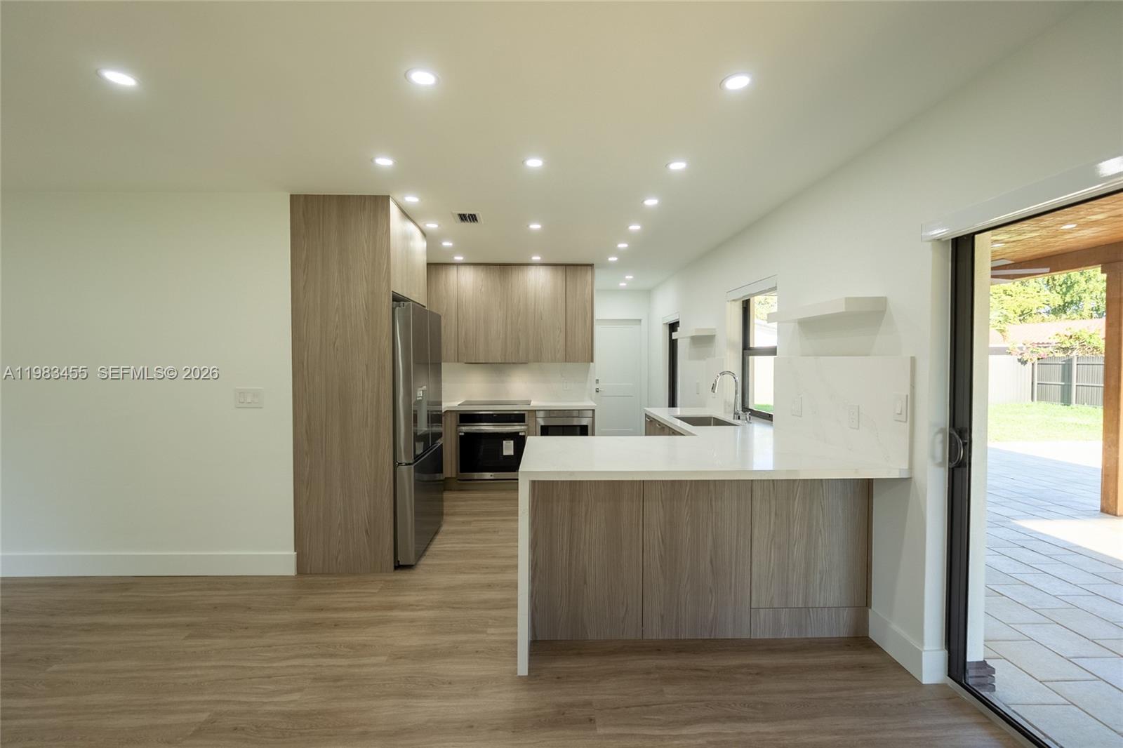 A modern kitchen features light wood cabinetry, stainless steel appliances, and a white quartz peninsula — 14515 Mahogany Ct, Miami Lakes FL 33014, MIAMI LAKES, FL