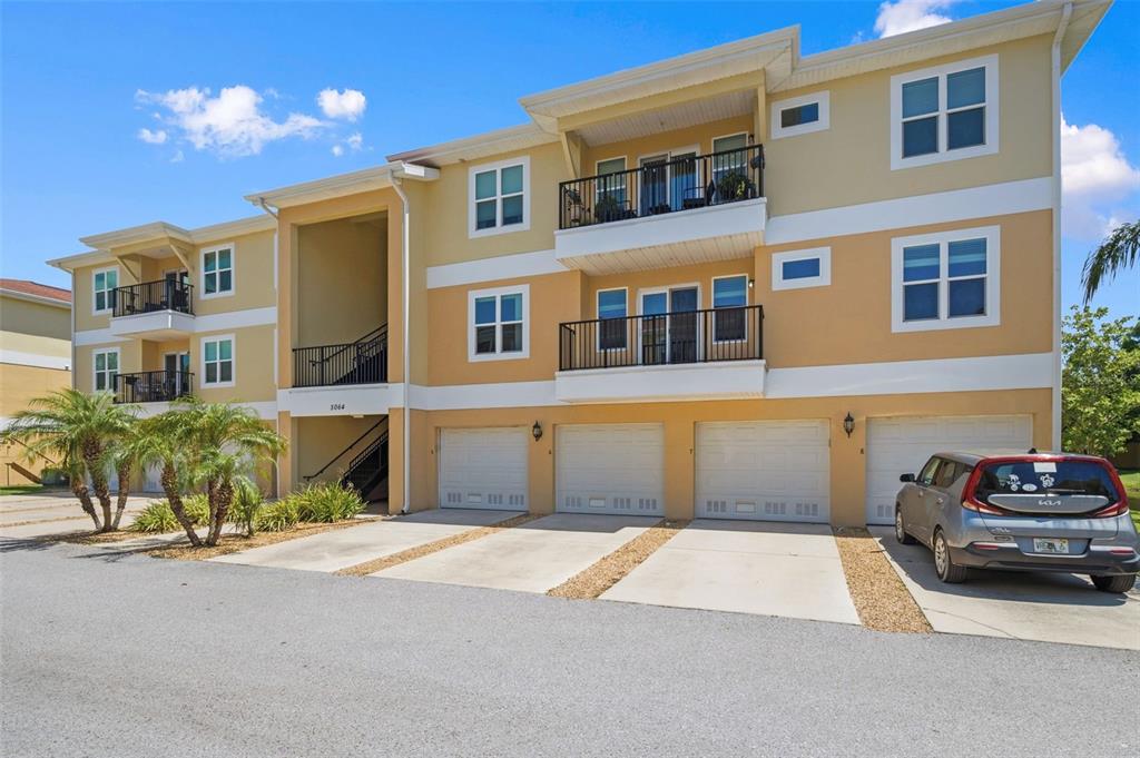 A three-story apartment building with tan stucco walls, balconies, and four ground-level garage doors — 5064 ROYAL PALMS WAY UNIT 204, NEW PORT RICHEY, FL
