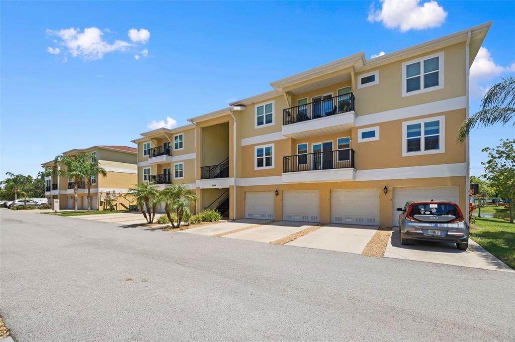 A three-story apartment building features tan stucco walls, multiple garage doors, and private balconies — 5064 ROYAL PALMS WAY UNIT 204, NEW PORT RICHEY, FL