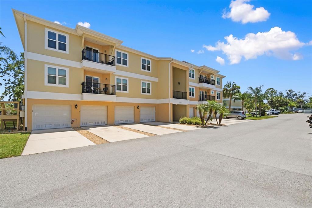 A three-story apartment building with yellow siding, multiple garage doors, and balconies — 5064 ROYAL PALMS WAY UNIT 204, NEW PORT RICHEY, FL