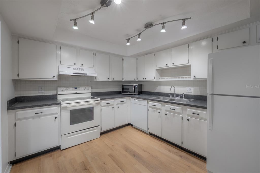 A kitchen features white cabinets, dark countertops, white appliances, and light wood-look flooring — 4681 1ST STREET NE UNIT 209, ST PETERSBURG, FL