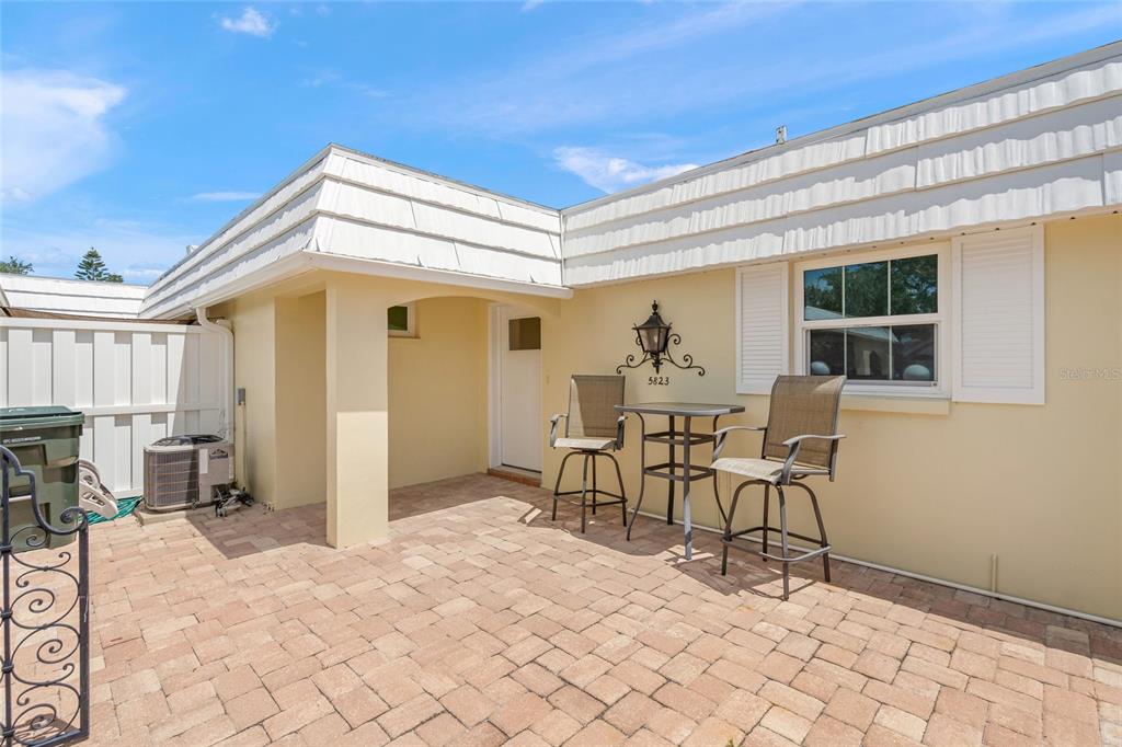 A paved patio features a small table and two chairs in front of a house — 5823 TIDEWOOD AVENUE UNIT 19, SARASOTA, FL