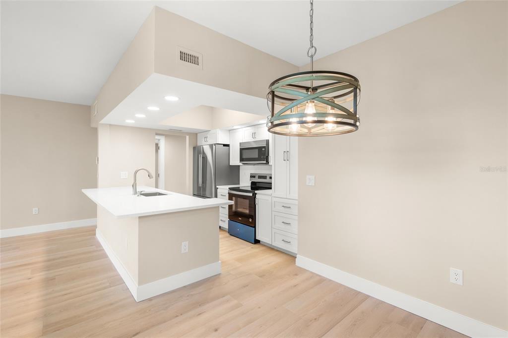 A kitchen features white cabinets, stainless steel appliances, a quartz island, and light wood flooring — 5823 TIDEWOOD AVENUE UNIT 19, SARASOTA, FL