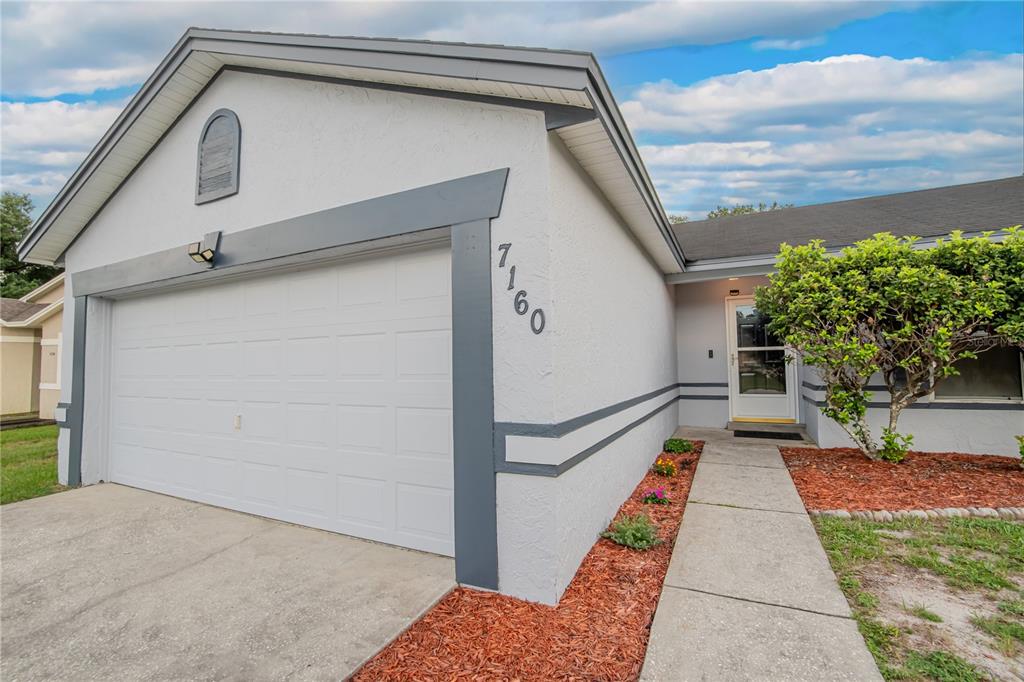A white house with a rear deck and a large grassy backyard under a cloudy sky — 7160 PEBBLE PASS LOOP, LAKELAND, FL