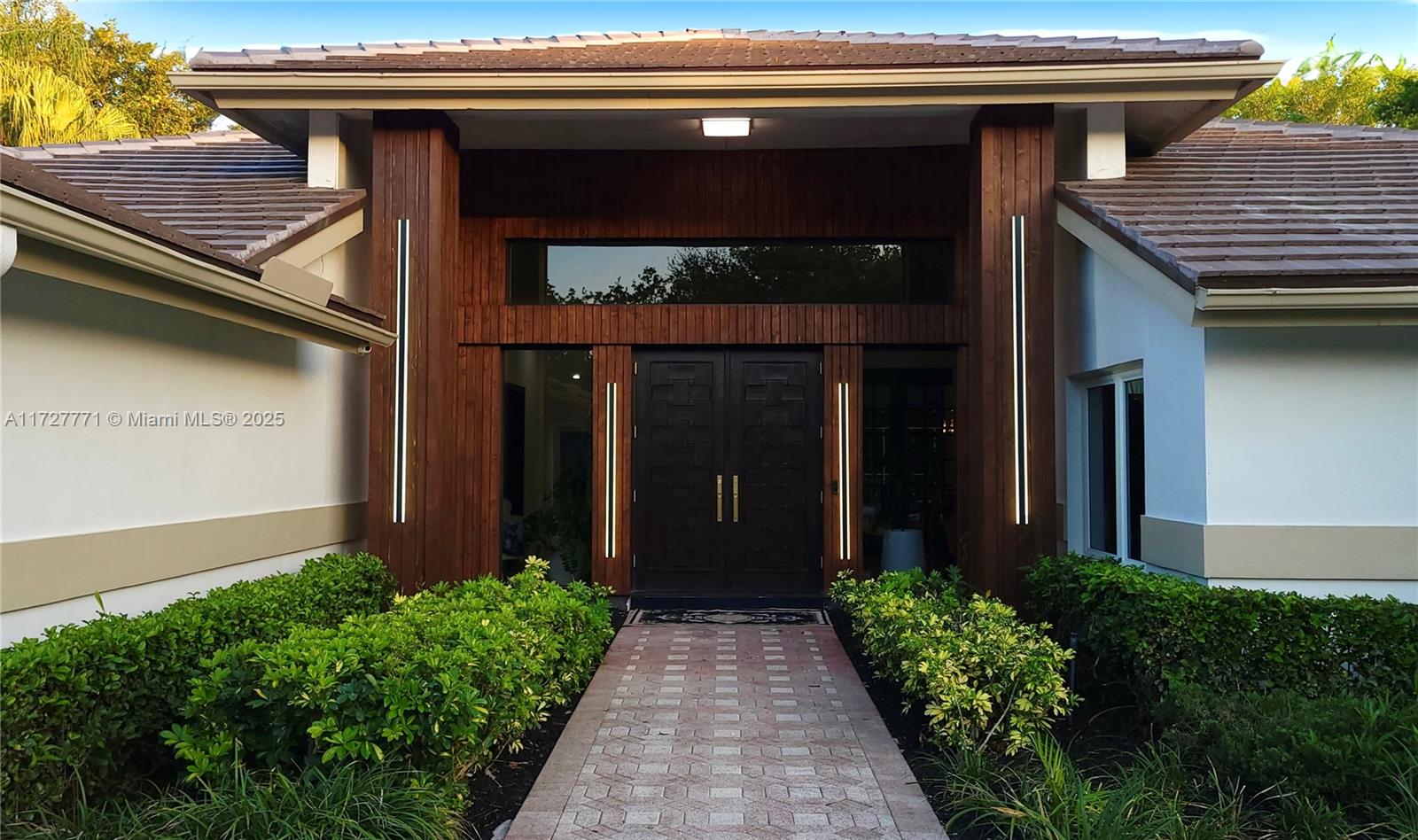 The exterior of a house features a brick walkway leading to a dark double-door entrance — 7700 S Woodridge Dr, Parkland FL 33067, PARKLAND, FL