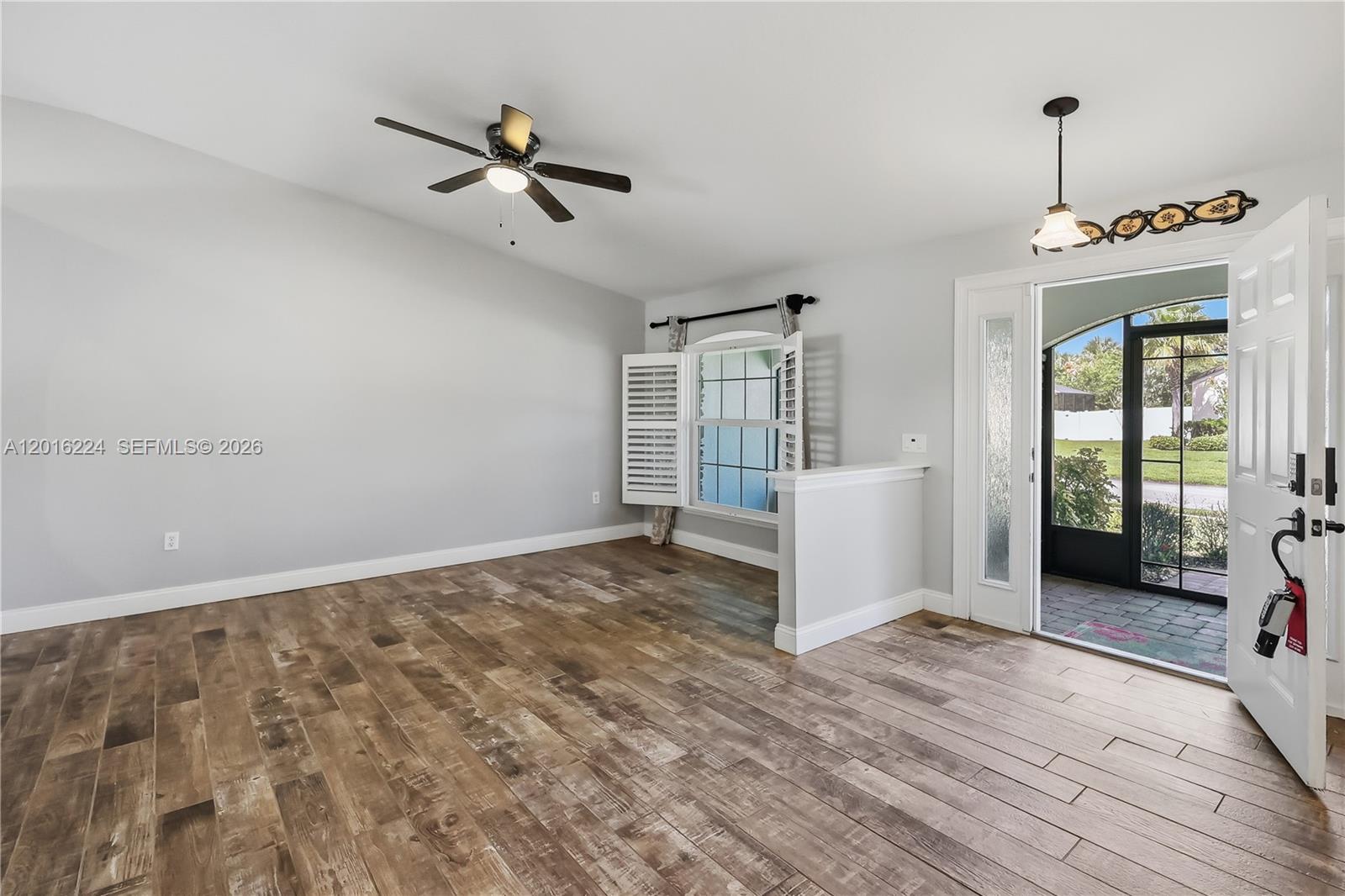 An empty room features wood-look tile flooring, a ceiling fan, and an open front door — 4738 Ashley Lake Cir, Vero Beach FL 32967, VERO BEACH, FL
