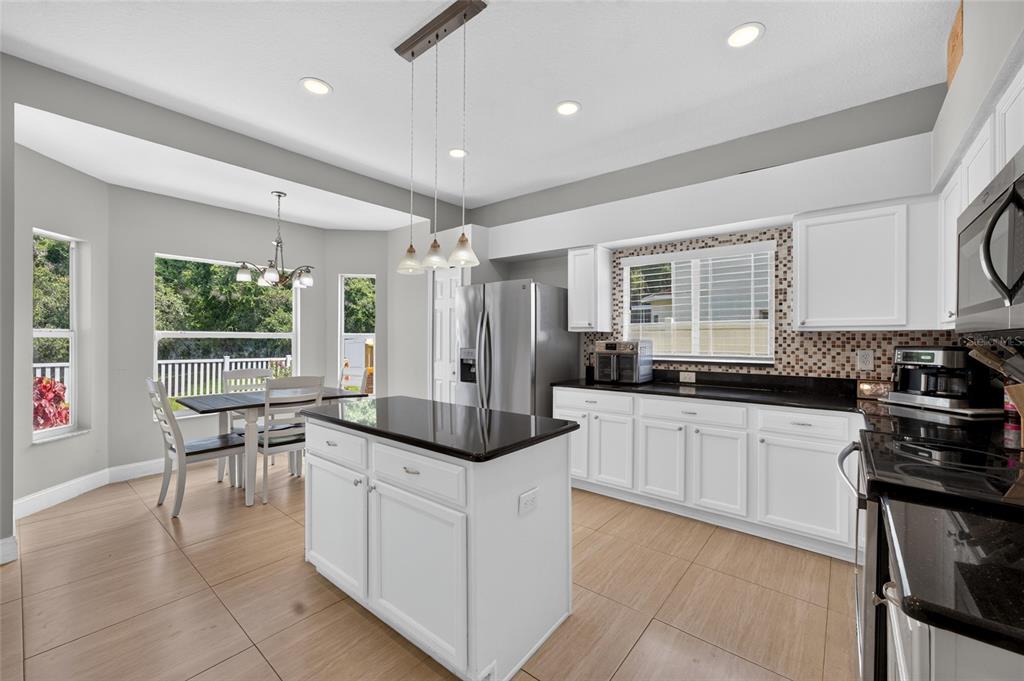 A kitchen with white cabinets, black countertops, a central island, and an adjacent dining area — 26943 CORAL SPRINGS DRIVE, WESLEY CHAPEL, FL
