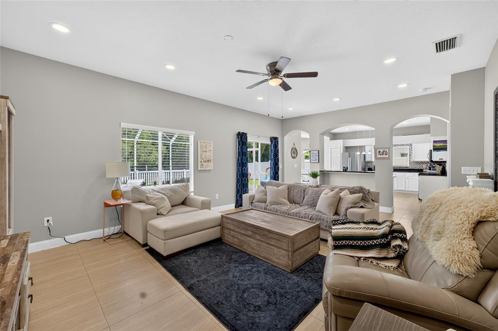 A living room with light tile floors, a dark area rug, and an open kitchen view — 26943 CORAL SPRINGS DRIVE, WESLEY CHAPEL, FL