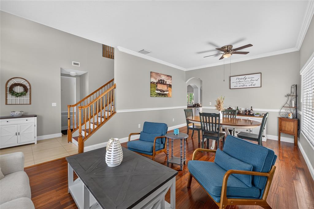 A living and dining room area features hardwood floors, blue armchairs, and a wooden staircase — 26943 CORAL SPRINGS DRIVE, WESLEY CHAPEL, FL