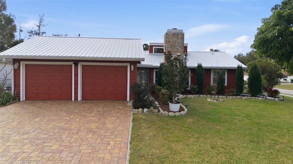 A red house with a metal roof, stone chimney, and a paved driveway — 980 BLUEBIRD TERRACE, DELTONA, FL