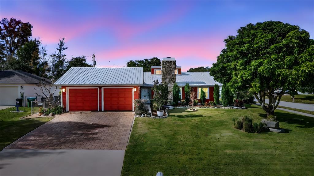 A single-story house with a metal roof, red garage doors, and a stone chimney — 980 BLUEBIRD TERRACE, DELTONA, FL