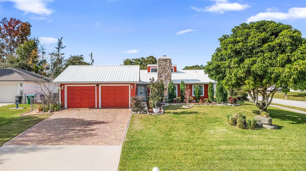 A single-story house with a red exterior, white metal roof, and stone chimney — 980 BLUEBIRD TERRACE, DELTONA, FL
