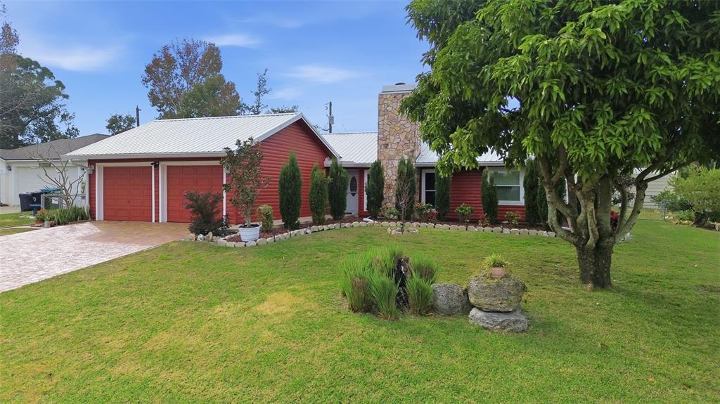 A red house with a metal roof, stone chimney, and a large tree in front — 980 BLUEBIRD TERRACE, DELTONA, FL