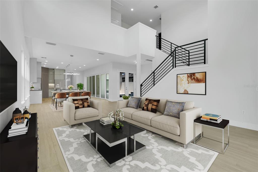A modern living room with a high ceiling, staircase, and open-concept kitchen in the background — 3036 KENSINGTON AVENUE, DAVENPORT, FL