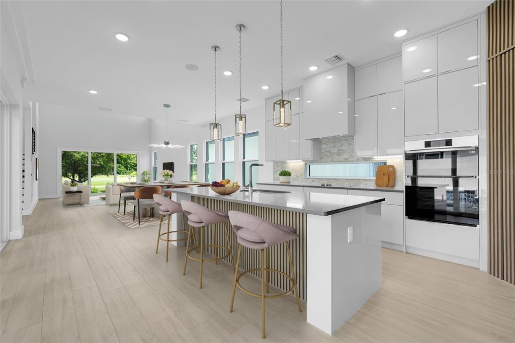 A modern kitchen features a large island with pink stools, white cabinetry, and wood accents — 3036 KENSINGTON AVENUE, DAVENPORT, FL