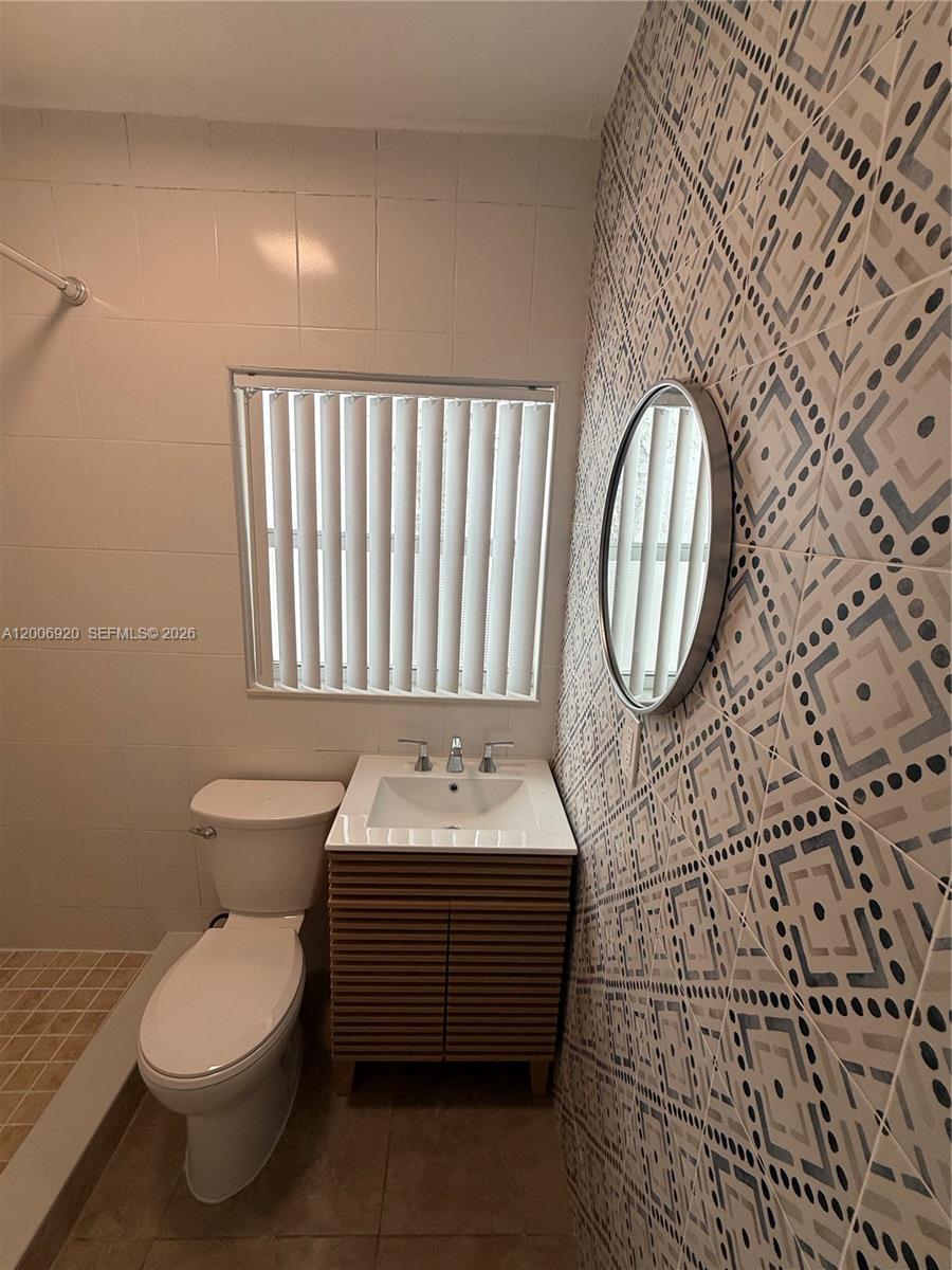 A bathroom features a patterned accent wall, a vanity, a toilet, and a shower area — 2816 Pine Tree Dr # 2, Miami Beach FL 33140, MIAMI BEACH, FL