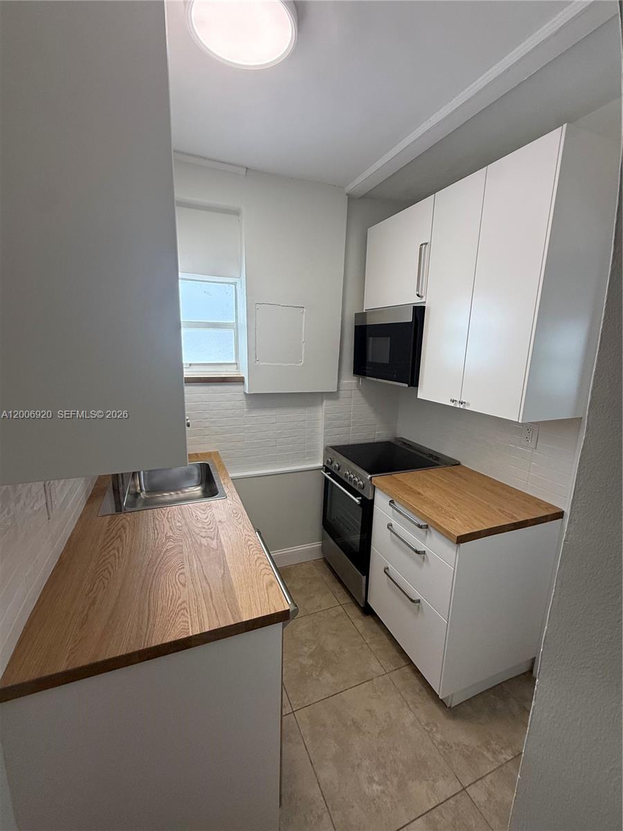 A small galley kitchen features white cabinets, wood countertops, and stainless steel appliances — 2816 Pine Tree Dr # 2, Miami Beach FL 33140, MIAMI BEACH, FL