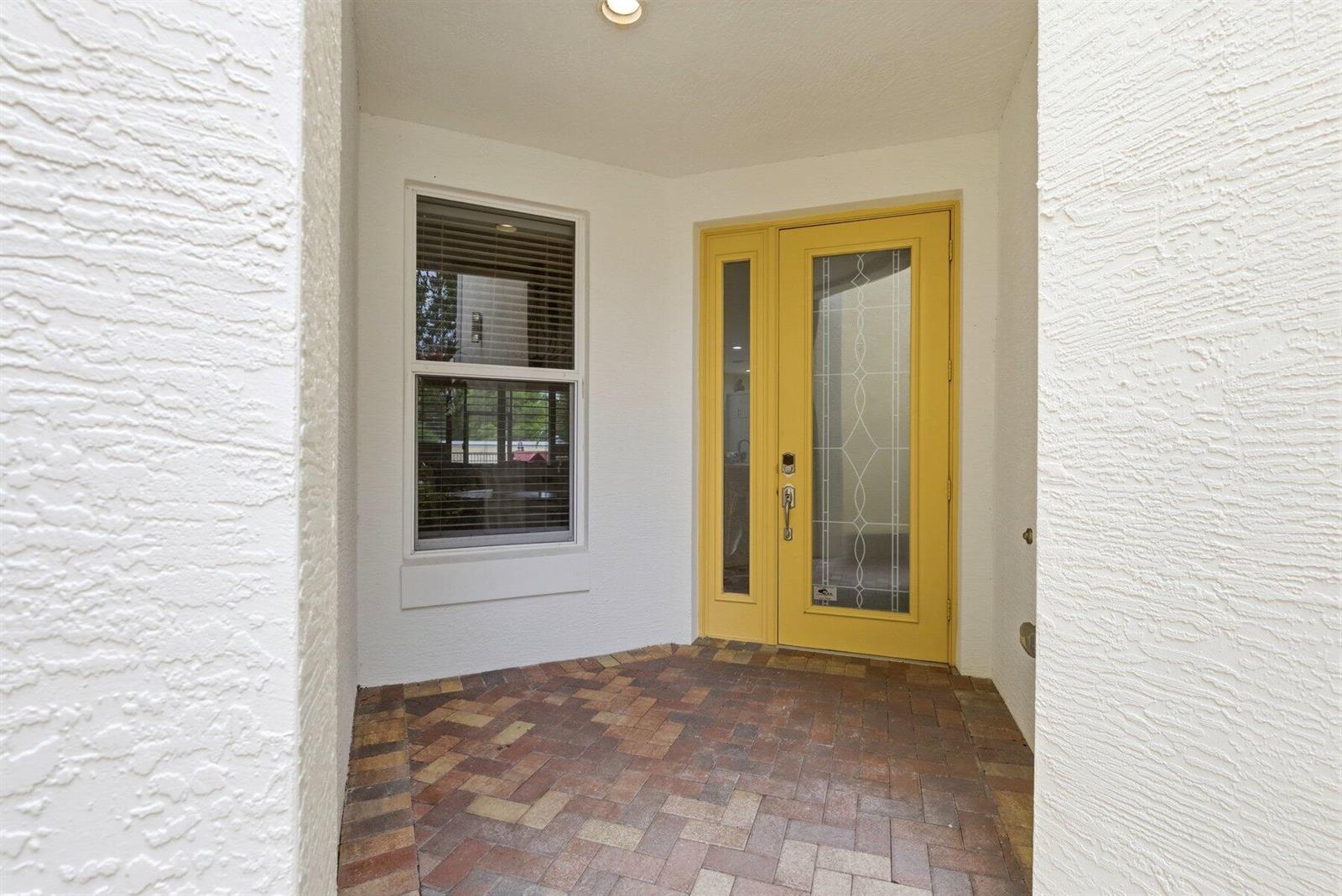 A yellow front door with a glass insert sits beside a window on a brick-paved porch — 4831 NW 16th Terrace, Boca Raton FL 33431, BOCA RATON, FL