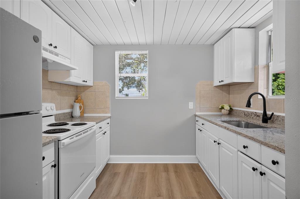 A galley kitchen features white cabinets, granite countertops, stainless steel appliances, and wood-look flooring — 2947 GILLESPIE AVENUE, SARASOTA, FL