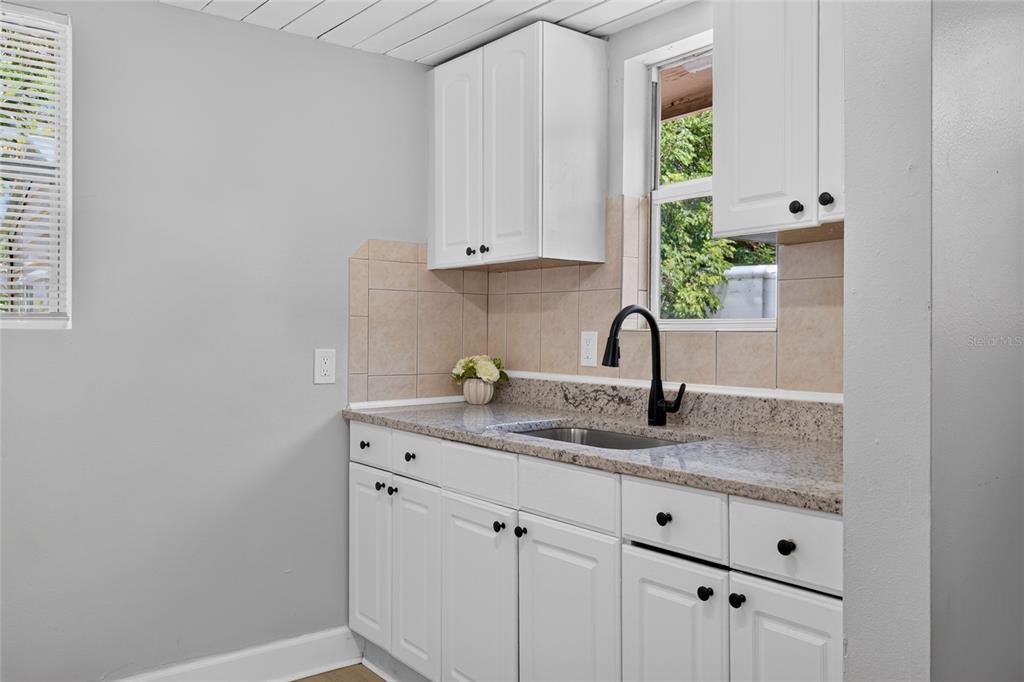 A kitchen features white cabinets, granite countertops, a black faucet, and a tiled backsplash — 2947 GILLESPIE AVENUE, SARASOTA, FL