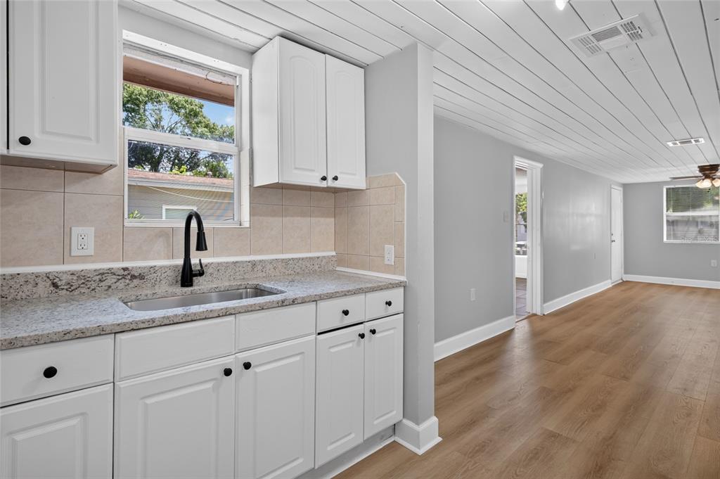 A kitchen with white cabinets, granite countertops, and a sink, opening into a living area — 2947 GILLESPIE AVENUE, SARASOTA, FL