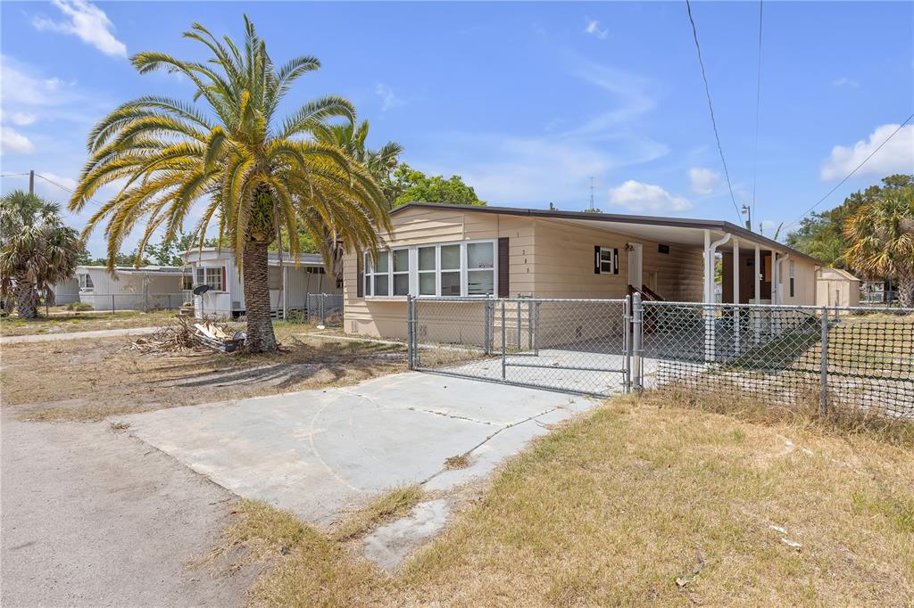 A single-story mobile home features a palm tree, a chain-link fence, and a concrete driveway — 11309 LEISURE LANE, PORT RICHEY, FL