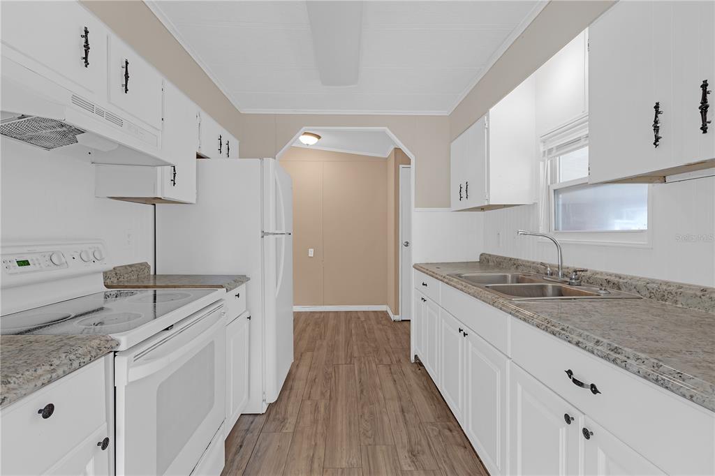 A kitchen with white cabinets, granite-look countertops, a white stove, and wood-look flooring — 11309 LEISURE LANE, PORT RICHEY, FL