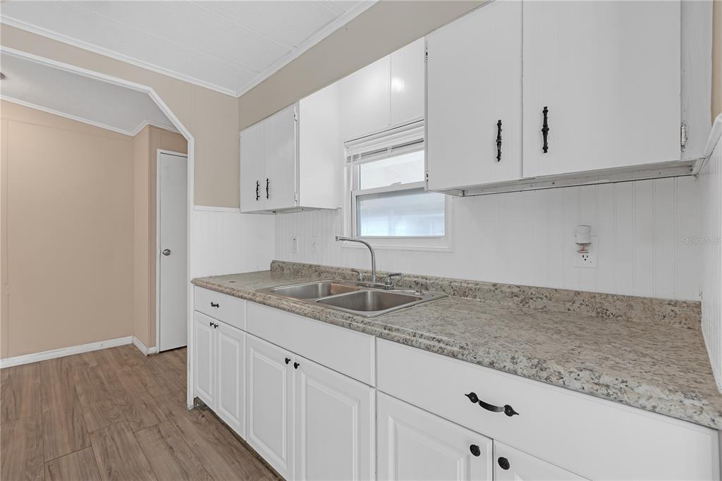 A kitchen features white cabinets, a speckled laminate countertop, a double sink, and wood flooring — 11309 LEISURE LANE, PORT RICHEY, FL
